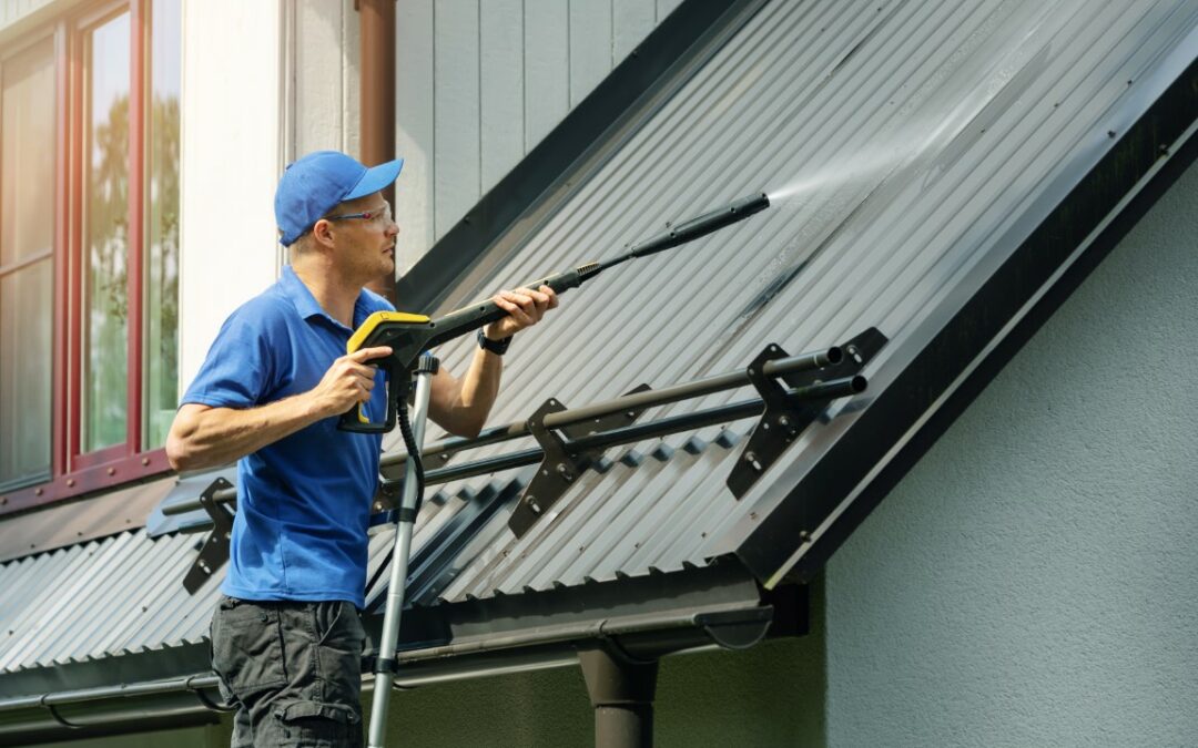 man standing on ladder and cleaning house metal roof with high p