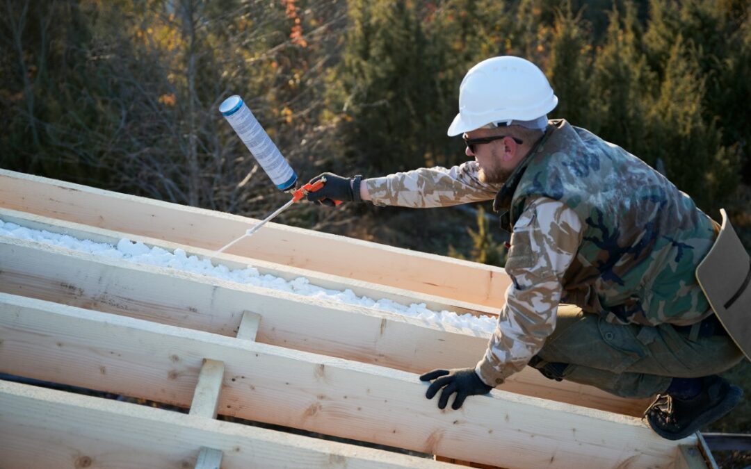 Male builder doing thermal insulation on roof of wooden frame house by polyurethane foam.